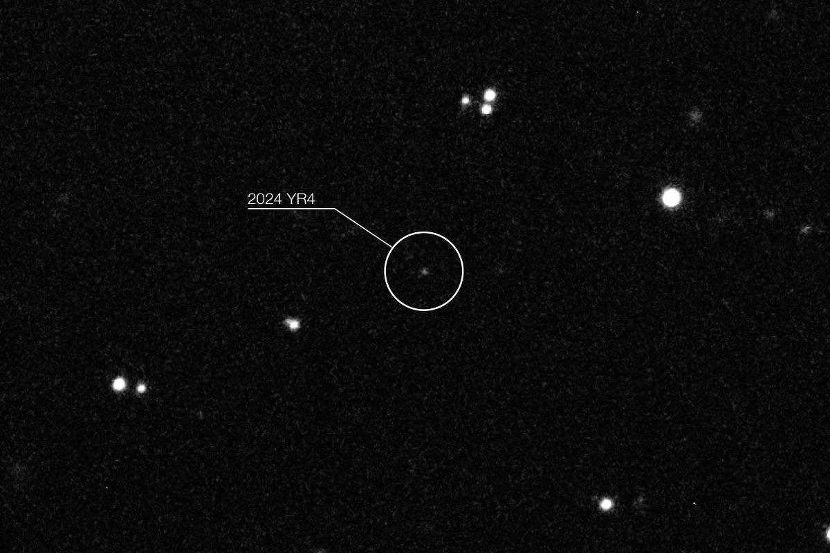 A imagem mostra um fundo escuro com várias estrelas visíveis. No centro, há um círculo branco que destaca o asteroide identificado como 2024 YR4, com uma linha apontando para ele. Outras estrelas estão espalhadas pelo fundo, algumas mais brilhantes e outras mais tênues.