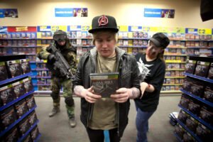 A imagem mostra uma cena em uma loja de jogos. Um jovem com cabelo loiro e um boné preto está segurando um jogo chamado