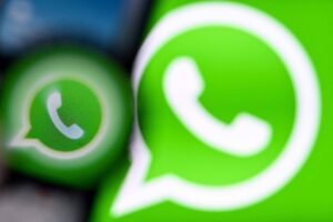 A imagem mostra o logotipo do WhatsApp em um fundo verde. O logotipo é composto por um balão de diálogo com um telefone dentro. A imagem está desfocada, com um efeito de desfoque que destaca o logotipo em primeiro plano.