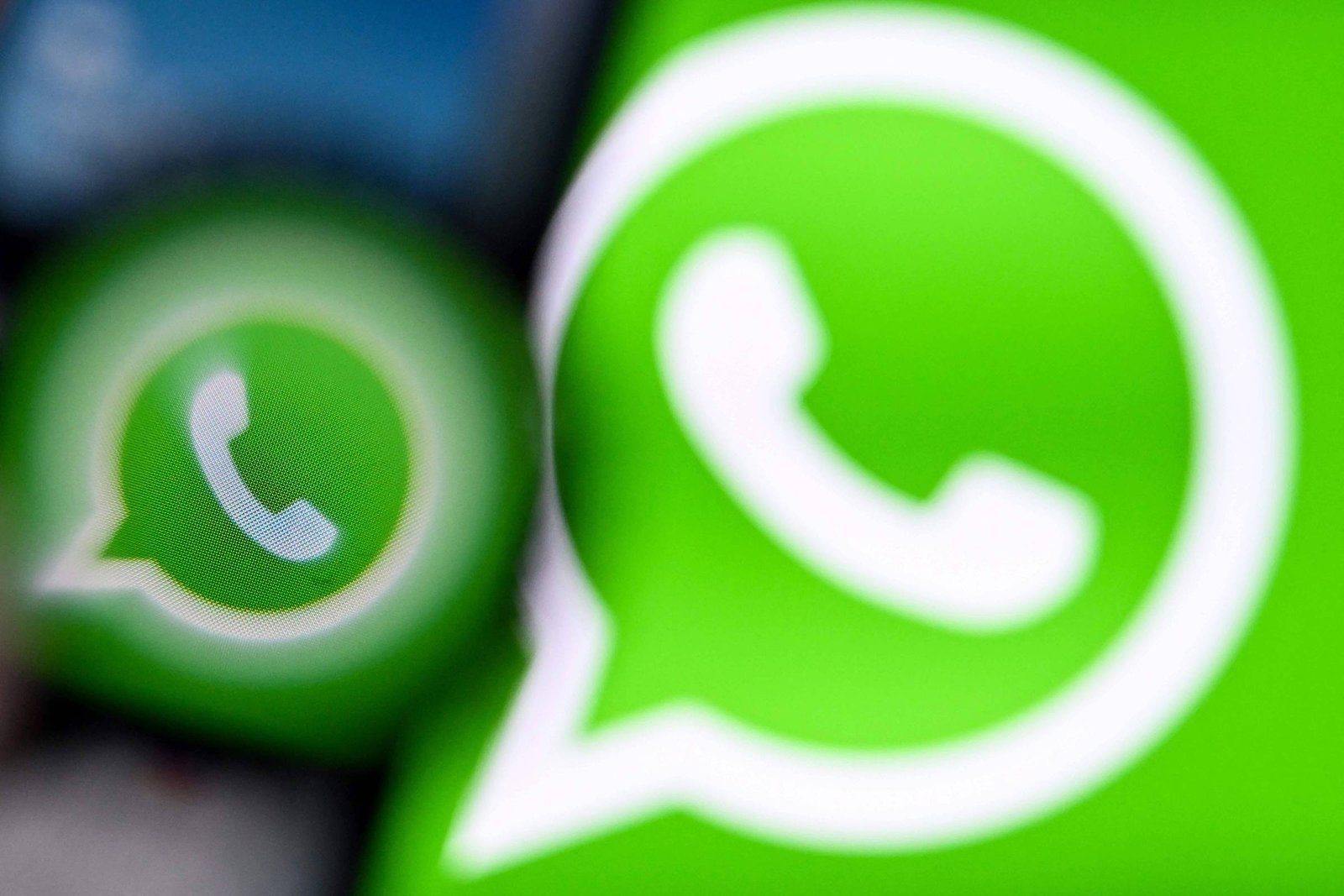 A imagem mostra o logotipo do WhatsApp em um fundo verde. O logotipo é composto por um balão de diálogo com um telefone dentro. A imagem está desfocada, com um efeito de desfoque que destaca o logotipo em primeiro plano.