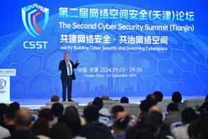 A imagem mostra um palestrante em um palco durante a Segunda Cúpula de Segurança Cibernética em Tianjin. O fundo exibe o logotipo da cúpula e informações sobre o evento, incluindo as datas de 3 a 5 de setembro de 2024. A plateia é visível, com várias pessoas assistindo à apresentação.