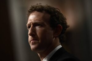 Um homem com cabelo castanho e ondulado, olhando para o lado com uma expressão séria. Ele está vestindo um terno escuro e uma camisa branca. O fundo é desfocado, sugerindo um ambiente formal.