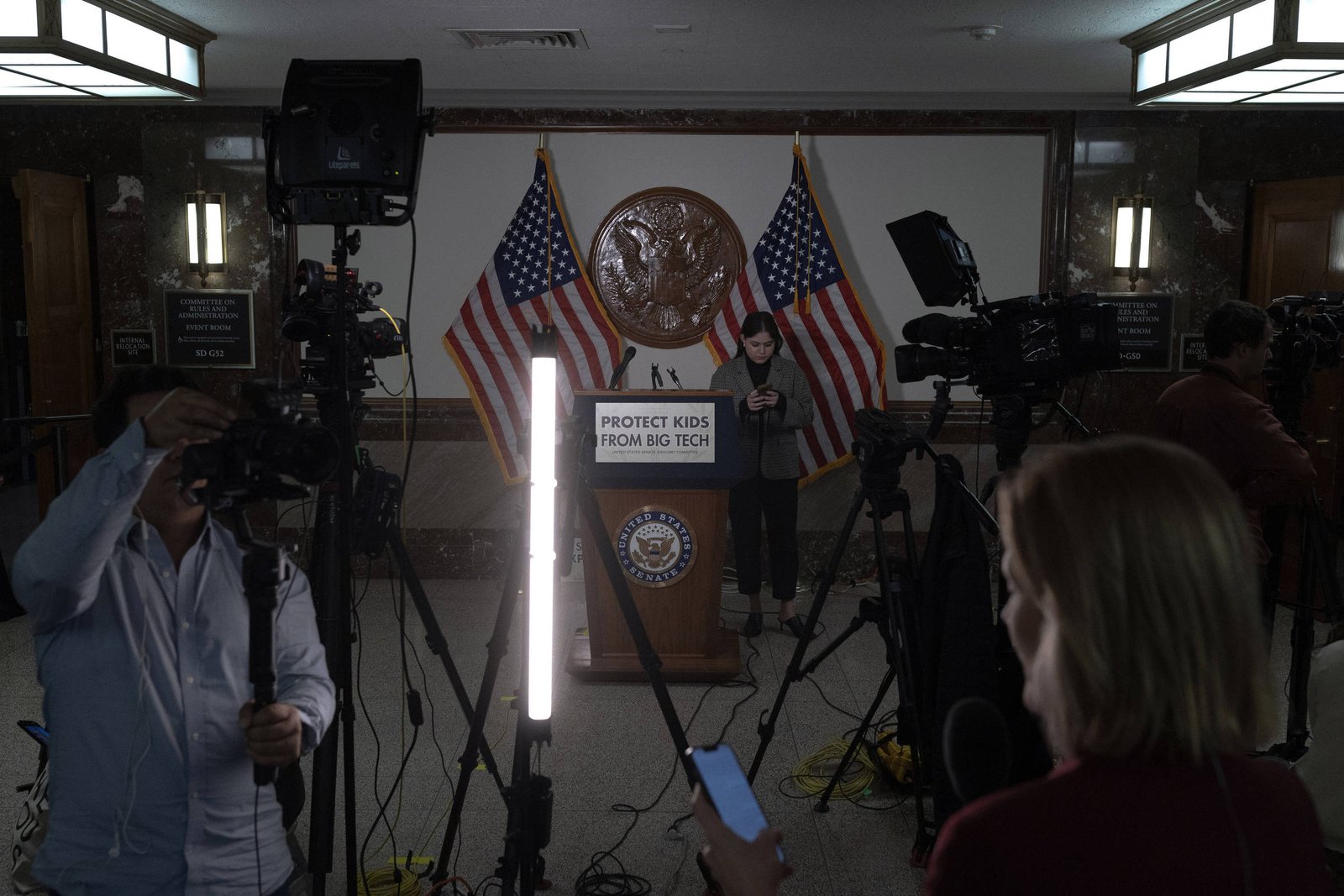 A imagem mostra um cenário de coletiva de imprensa com um púlpito central, onde está escrito