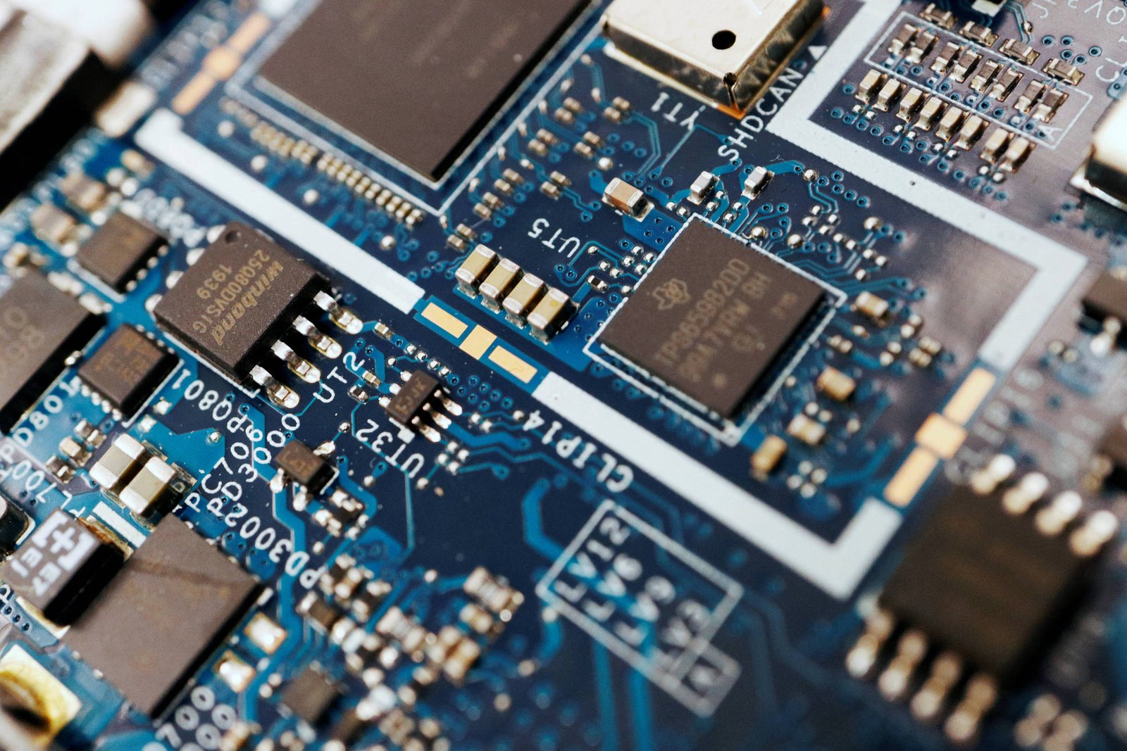 A imagem mostra uma placa de circuito impresso com diversos componentes eletrônicos. Há chips, resistores e conectores visíveis, todos dispostos sobre um fundo azul. Os circuitos são complexos e interconectados, com detalhes em dourado e prateado.