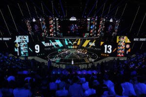 Arena de eSports com público assistindo partida entre Gen.G Esports e AGAL. Placar mostra 9 a 13 para AGAL, com jogadores nas estações e telas grandes exibindo o jogo.