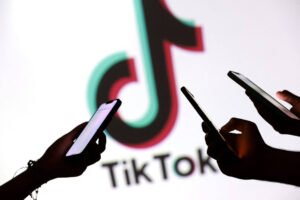 Três mãos seguram celulares com telas iluminadas em frente a uma tela branca exibindo o logo colorido do TikTok e o nome da plataforma em preto.