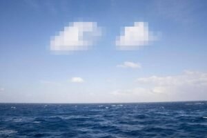 Vista do mar aberto com ondas pequenas e céu azul claro com algumas nuvens dispersas.