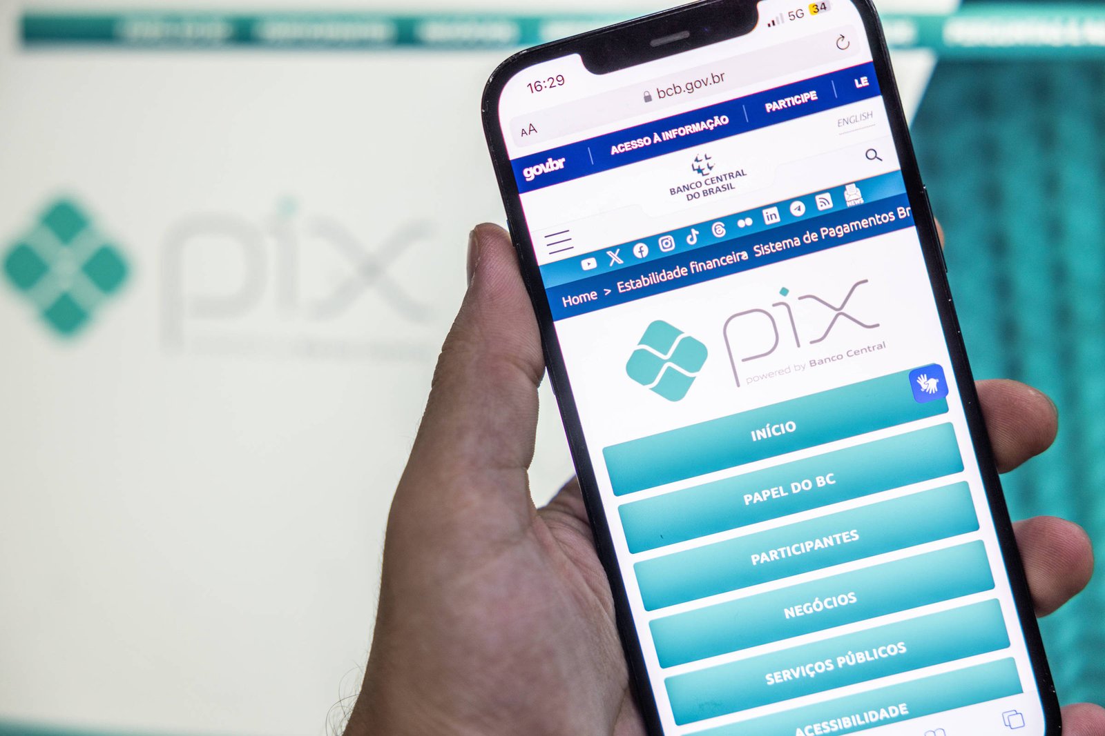 A imagem mostra uma mão segurando um smartphone que exibe a interface do aplicativo Pix. Na tela do celular, é possível ver o logotipo do Pix e opções como
