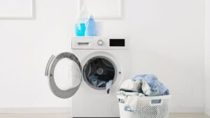 Máquina de lavar com produtos na parte de cima e um cesto de roupas sujas. A máquina está com a tampa aberta.