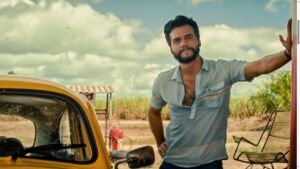 Wagner Moura encostado em uma parede ao lado de um carro