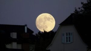 Foto da lua cheia com silhuetas de casas grandes na frente