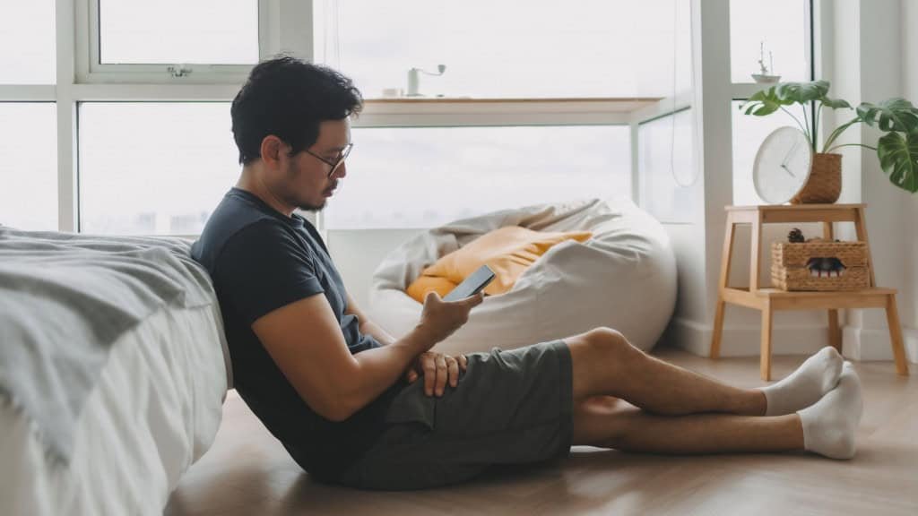 Homem sentado no chão de apartamento usando celular