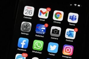 Tela de smartphone exibe ícones de aplicativos organizados em quatro linhas, incluindo WhatsApp, Instagram, Facebook, YouTube, Gmail e Google Maps, sobre fundo preto.