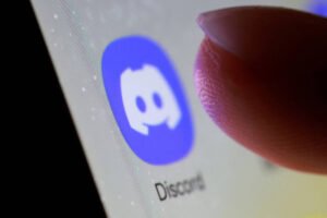 Dedo indicador próximo ao ícone azul do aplicativo Discord em uma tela de smartphone, com o nome