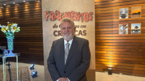 Autor durante o lançamento do livro Fragmentos do Cotidiano em Crônicas, em ambiente interno, posando diante do painel do evento