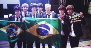 integrantes-do-bts-segurando-bandeira-do-brasil-durante-ou-show-usando-ternos-e-sorrindo-em-palco