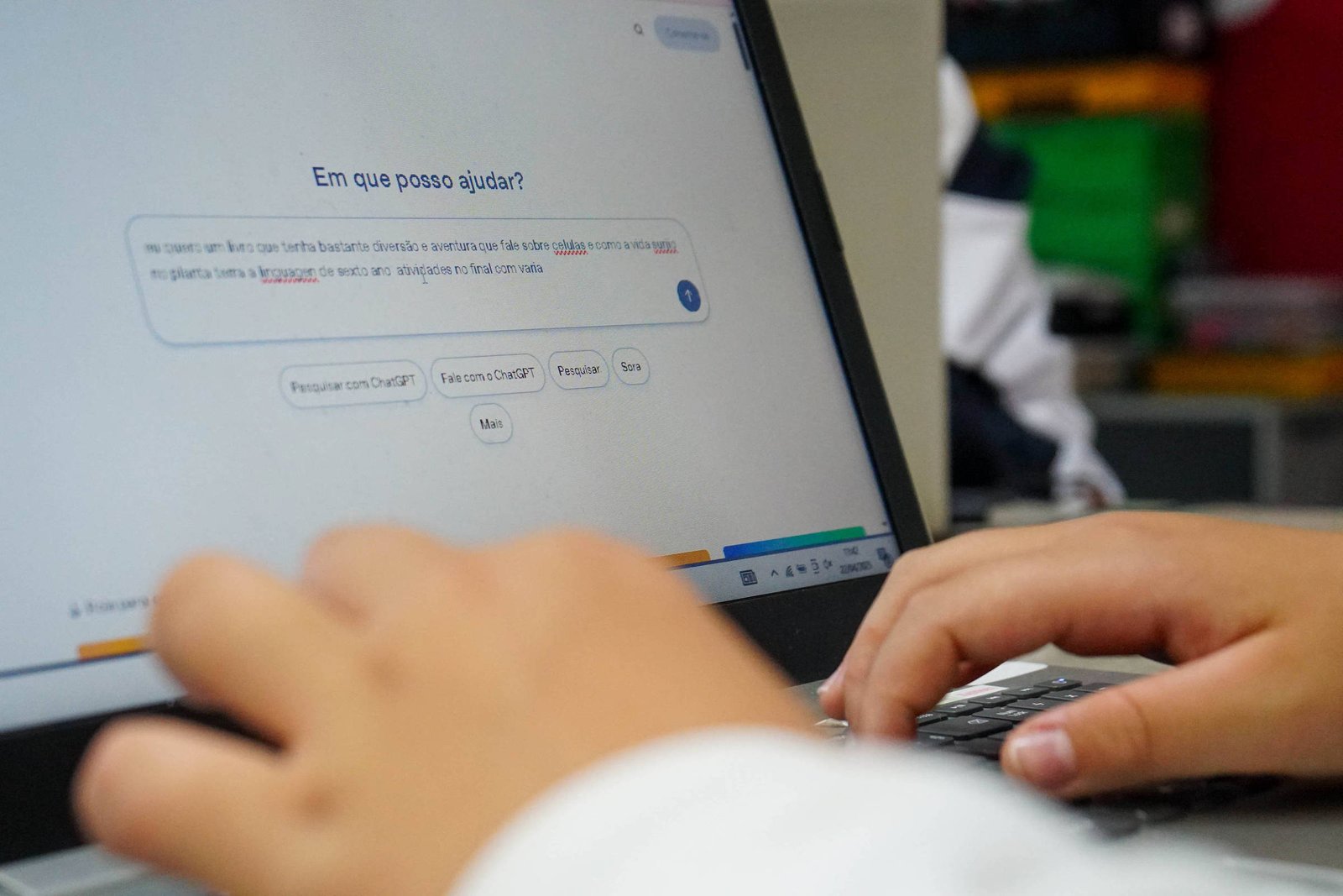 Mãos de uma pessoa digitando em teclado de laptop Lenovo. Tela exibe assistente virtual com texto em português perguntando