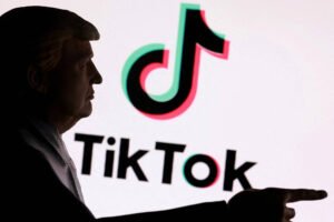 Silhueta de homem de perfil apontando com a mão direita para o logo colorido do TikTok em fundo branco.