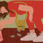 Mulher agachada vestindo roupa vermelha e tênis brancos, recolhendo moedas que caem de sua bolsa amarela no chão marrom.