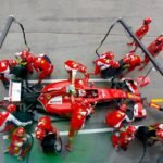 Equipe de Fórmula 1 realiza pit stop durante corrida com carro cercado por mecânicos