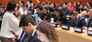 Um grupo diversificado de jovens participantes do Fórum da Juventude do ECOSOC na Sede das Nações Unidas, sentados em um auditório com crachás.