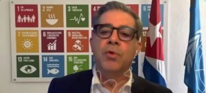 Francisco Pichon, Coordenador Residente em Cuba, fala aos jornalistas sobre a situação no país, diante de um cartaz dos Objetivos de Desenvolvimento Sustentável da ONU e das bandeiras de Cuba e da ONU.