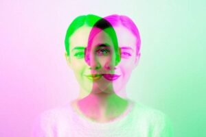 Mulher de cabelos presos e blusa clara aparece com três sobreposições translúcidas em verde, rosa e roxo, criando efeito visual de múltiplas faces.