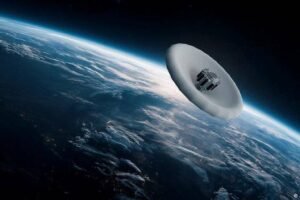 Satélite com formato circular e estrutura central visível orbita acima da Terra, que mostra nuvens e a curvatura do planeta contra o espaço escuro.