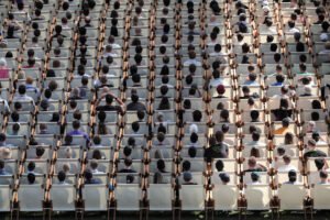 Pessoas sentadas em cadeiras brancas em um gramado.