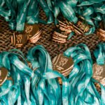Várias medalhas de corrida douradas e prateadas com fitas azuis estão organizadas lado a lado sobre uma superfície texturizada.