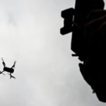 Silhueta de pessoa segurando controle e de drone no céu