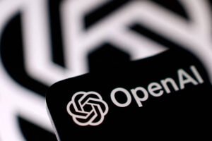 Logotipo branco da OpenAI com texto ao lado exibido em tela escura de dispositivo móvel. Fundo desfocado mostra padrão semelhante ao logotipo em preto e branco.
