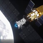 Satélite com painéis solares grandes e escuros estendidos em órbita ao redor da Terra, que aparece parcialmente iluminada com nuvens visíveis. O satélite tem estrutura metálica e componentes dourados refletindo luz.