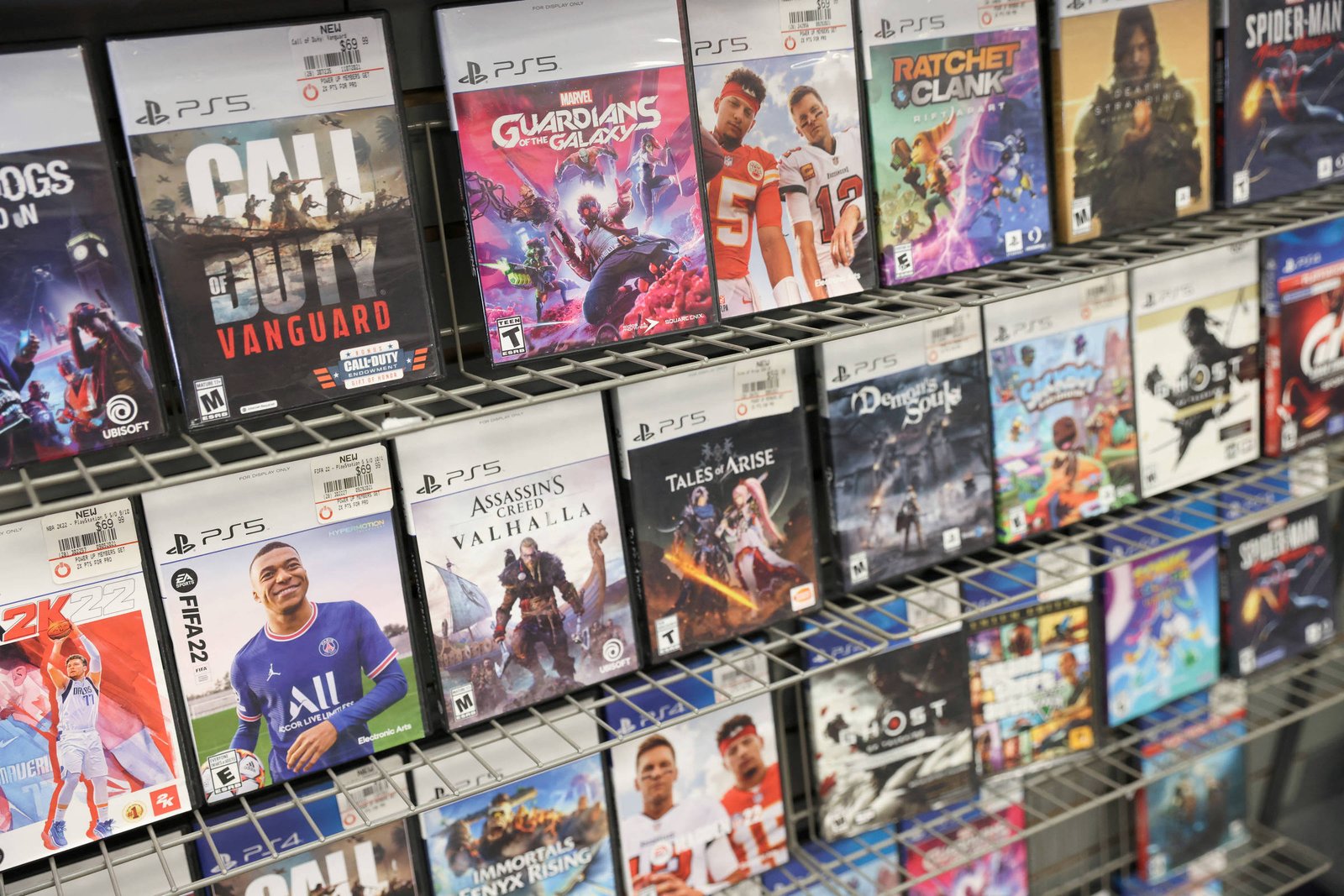 Diversas capas de jogos para PlayStation 5 organizadas em prateleiras metálicas. Entre os títulos visíveis estão Call of Duty Vanguard, Marvel