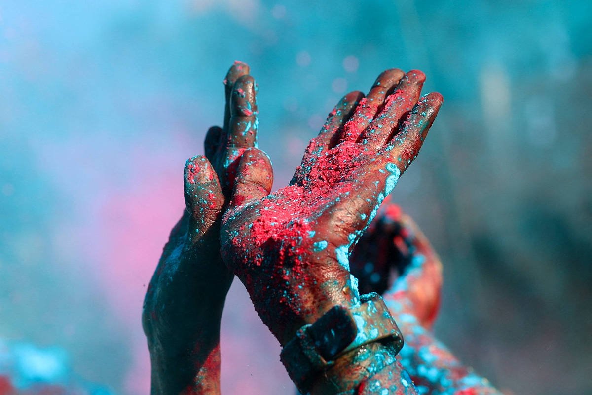 Duas mãos levantadas cobertas por pó colorido vermelho e azul, com fundo desfocado em tons semelhantes.
