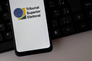 Logotipo do Tribunal Superior Eleitoral (TSE) exibido na tela de um smartphone sobre um teclado de computador.