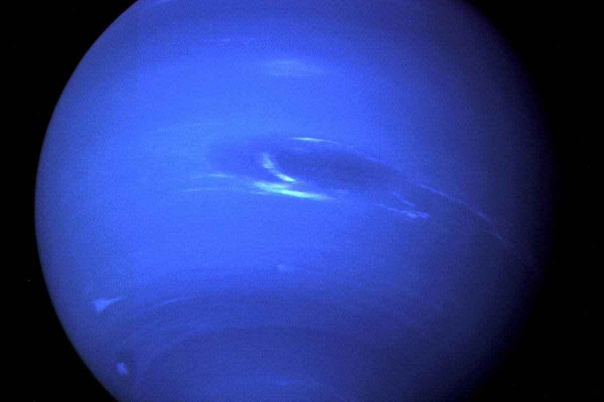 Imagem do planeta Netuno mostrando sua coloração azul intensa com faixas claras e uma mancha escura visível no hemisfério superior direito. O fundo é completamente preto, destacando o planeta.