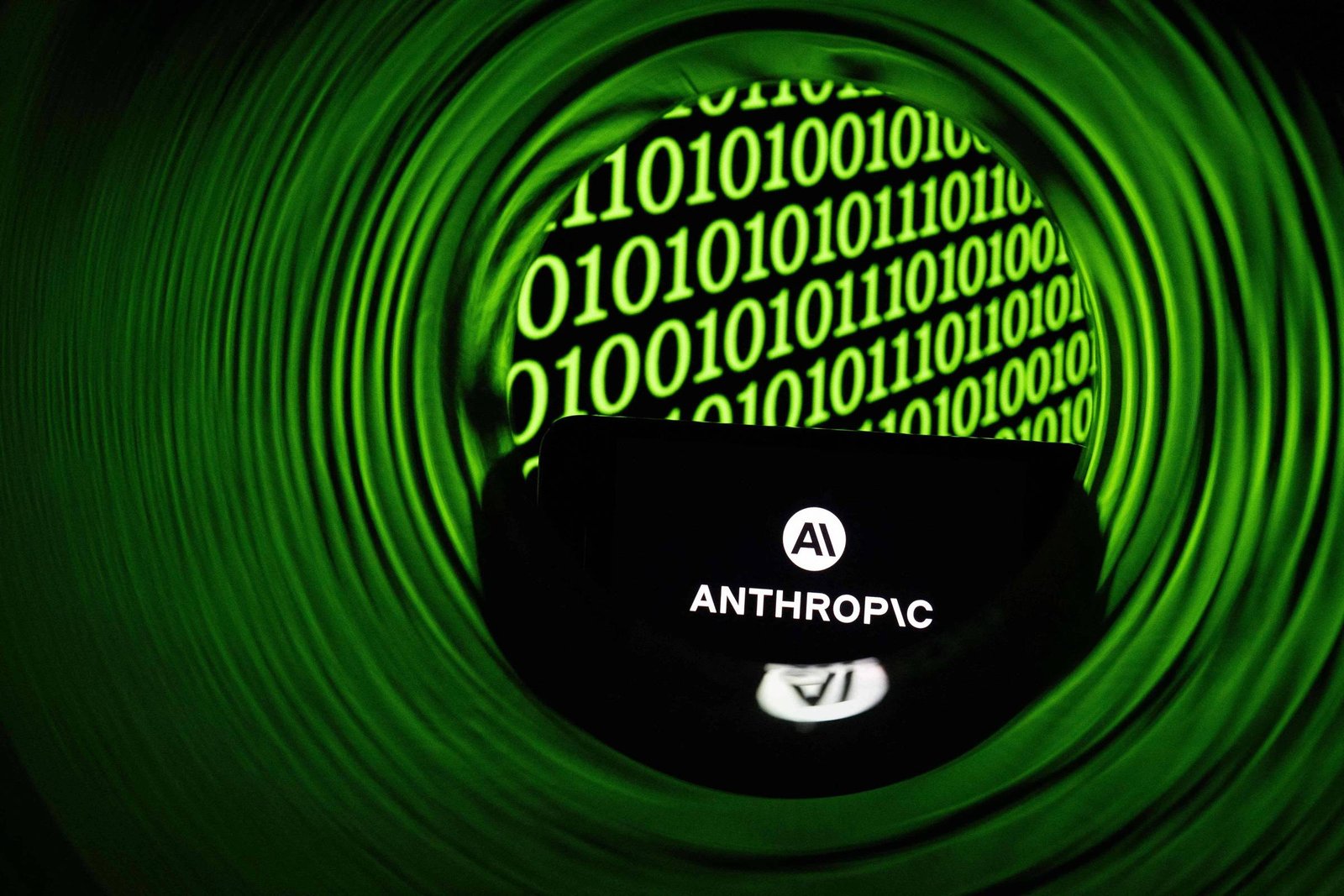 Logotipo branco da Anthropic em fundo preto, visto através de um tubo verde circular. Ao fundo, código binário verde com números 0 e 1 em sequência.