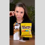 Mulher de cabelos castanhos e lisos segura embalagem amarela de M&M