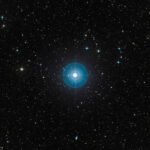 Estrela azul intensa no centro da imagem cercada por inúmeras estrelas menores em fundo negro do espaço.