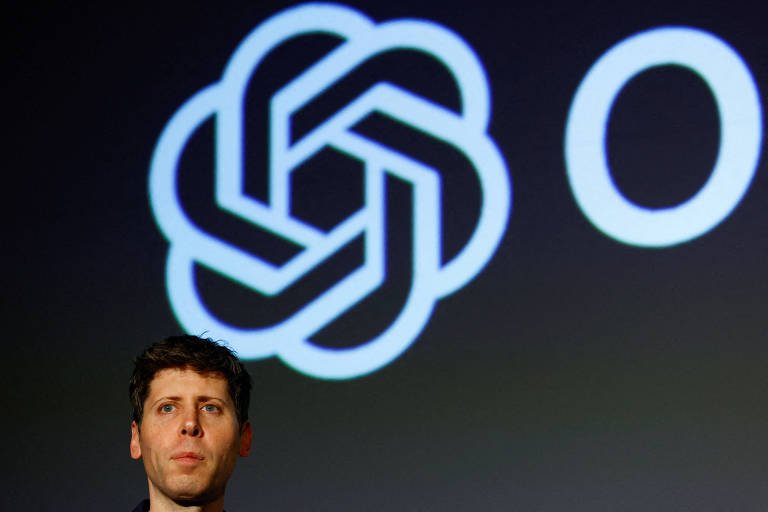 Homem de cabelo curto e expressão séria está em primeiro plano com fundo escuro. Atrás dele, grande logotipo branco da OpenAI aparece iluminado.