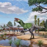 Vários dinossauros caminham próximos a um lago em uma paisagem com árvores e plantas. Um dinossauro verde com boca aberta está em destaque à direita, enquanto outros dinossauros maiores e menores estão ao fundo, sob céu parcialmente nublado.